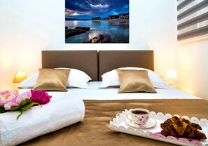 A neatly made bed with white and beige pillows, a tray with a cup of coffee and a croissant, and a bouquet of flowers. - Adria Croatica (Omis)