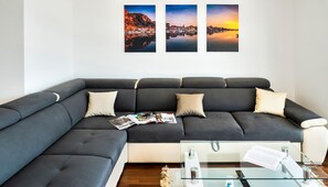 Ett modernt vardagsrum med en grå hörnsoffa, ett soffbord i glas och tre inramade fotografier på väggen.