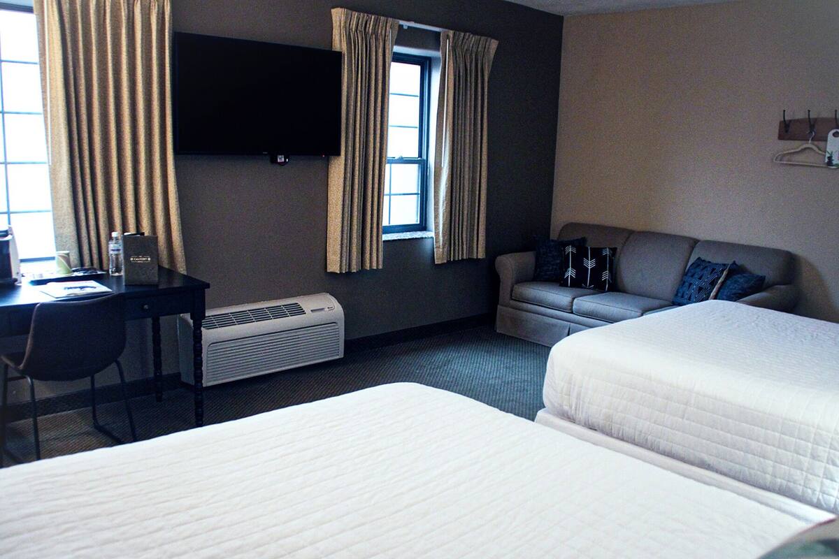A hotel room with two beds, a desk, a chair, a TV mounted on the wall, and a window with curtains.
