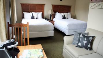 A hotel room with two beds, a wooden chair, a small table with a map, and a sofa with a pillow.