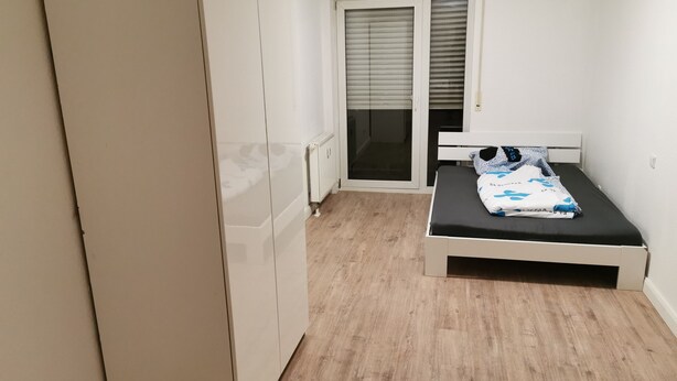 A bedroom with a bed, a wardrobe, and a sliding glass door leading to a balcony. - Nice Flat near Town Center & Wöhrder See (Nuremberg)