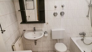 A bathroom with a white sink, toilet, and bathtub, a mirror above the sink, and a radiator on the left. - Nice Flat near Town Center & Wöhrder See (Nuremberg)