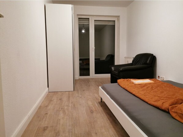 A bedroom with a bed, a chair, a wardrobe, and a sliding door leading to a balcony.