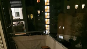 A balcony with a small stool, a metal railing, and a view of neighboring buildings at night. - Nice Flat near Town Center & Wöhrder See (Nuremberg)
