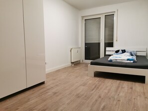 Ein Schlafzimmer mit Bett, Schrank, Heizkörper und einer Schiebetür.