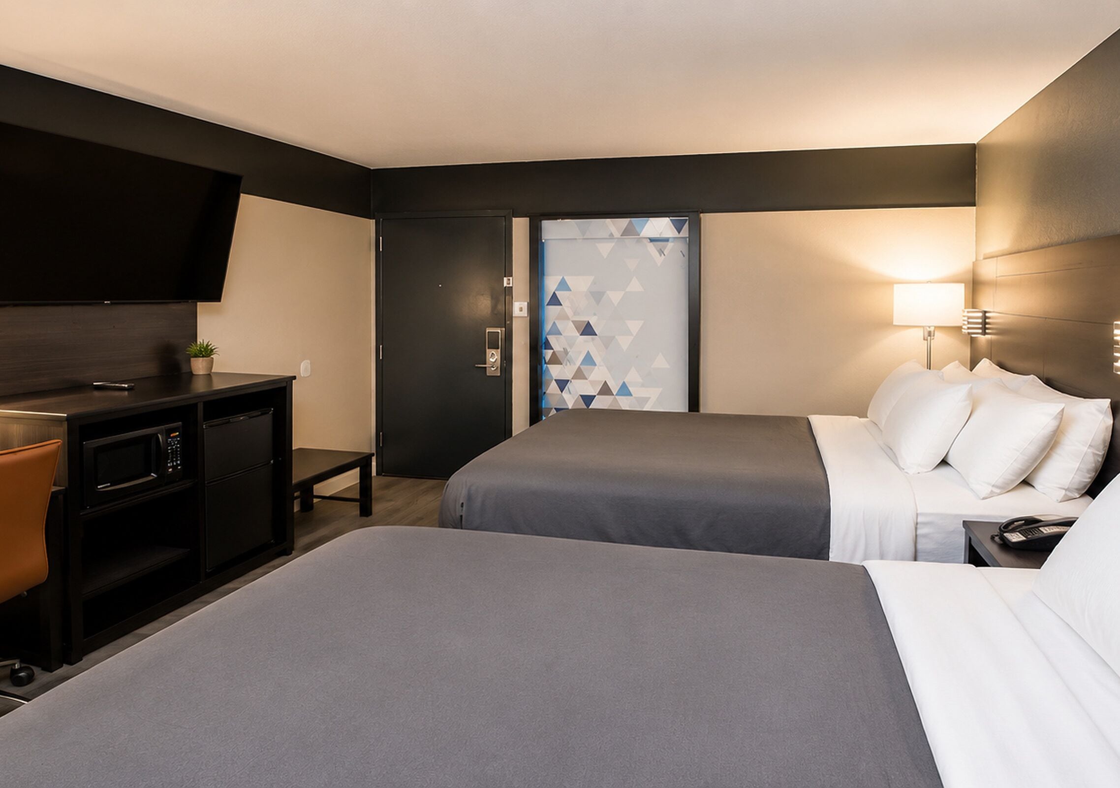 Habitación de hotel con dos camas, un escritorio con microondas, un televisor y una puerta con diseño geométrico.