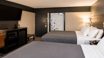 Habitación de hotel con dos camas, un escritorio con microondas, un televisor y una puerta con diseño geométrico.