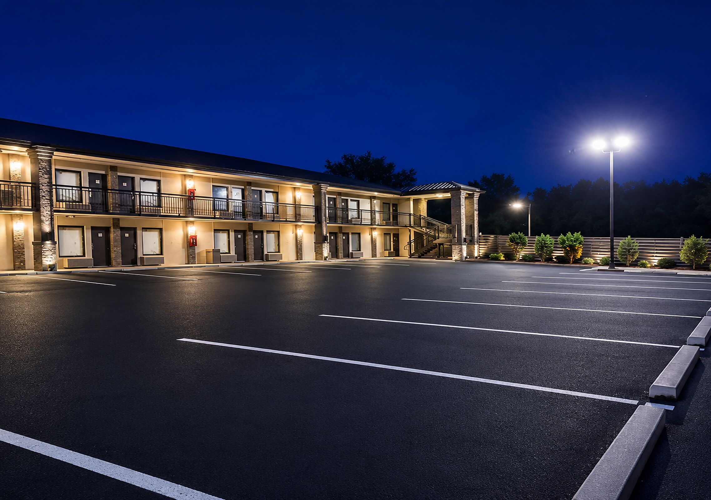 A multi-story motel with a parking lot, exterior lighting, and a staircase leading to the entrance.
