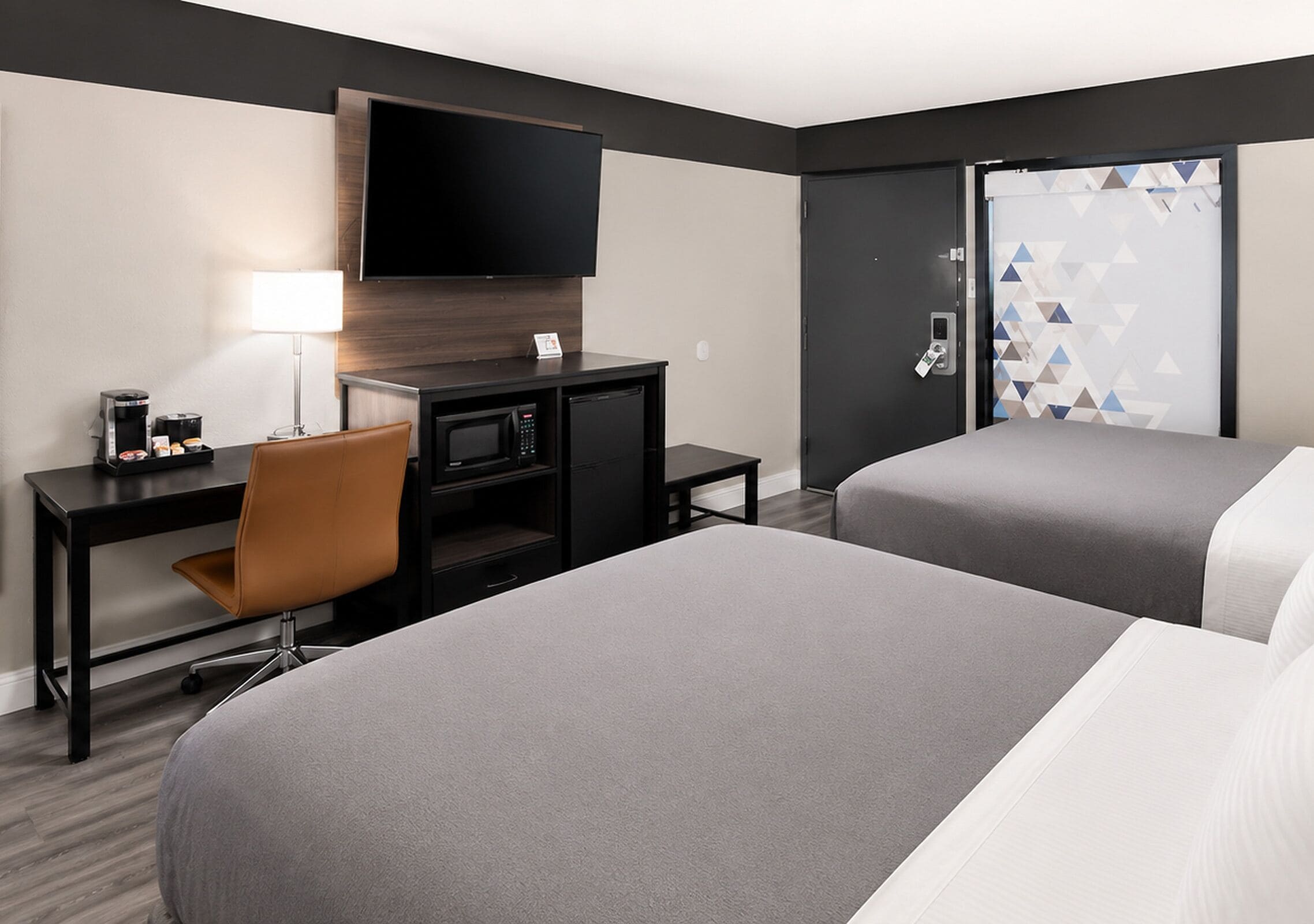 A hotel room with two beds, a desk with a chair, a flat-screen TV, a coffee maker, and a microwave.