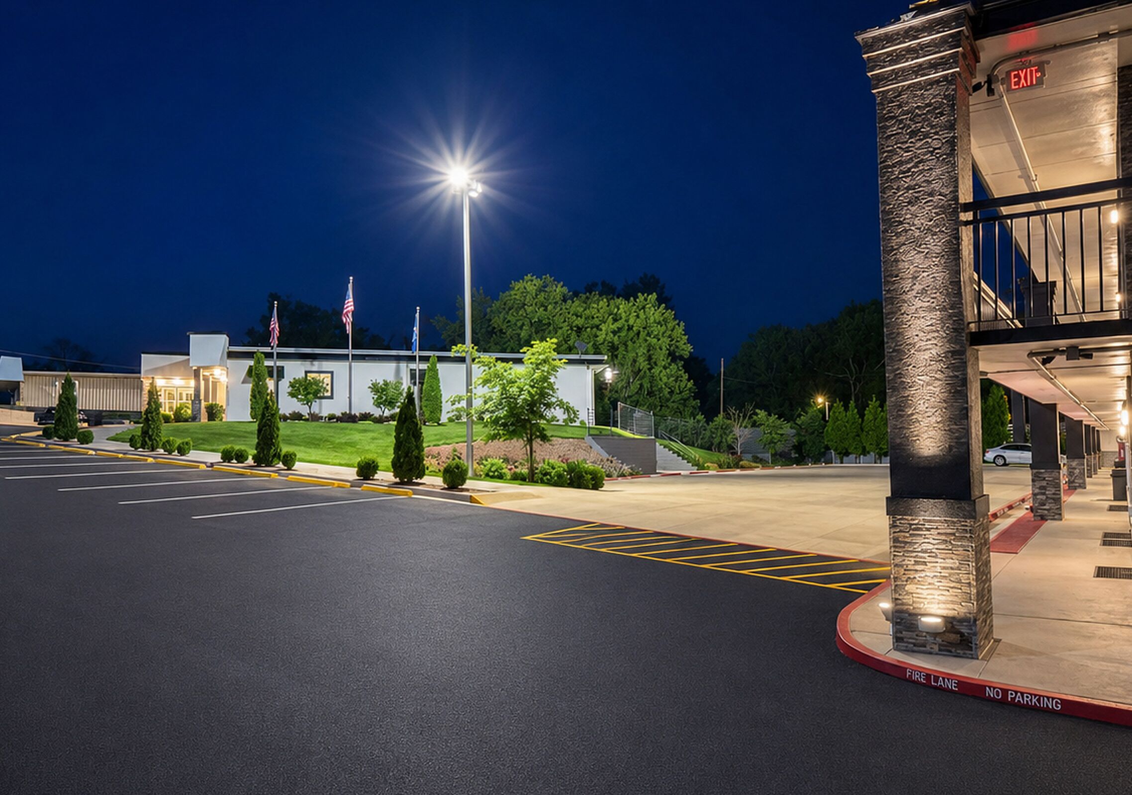 A parking lot with marked fire lanes and no parking signs, a building entrance with an exit sign, and a well-lit street.