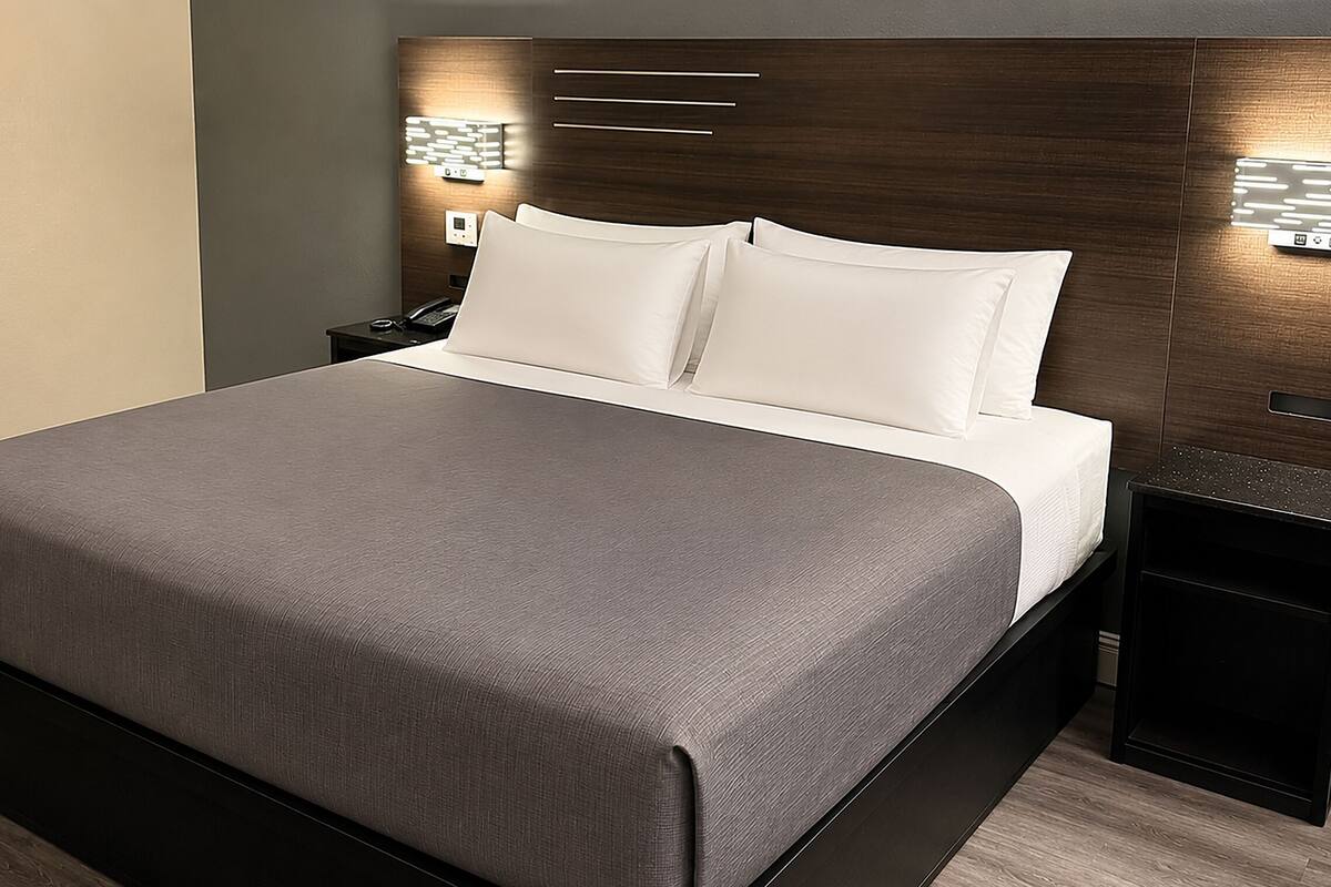 Une chambre d’hôtel moderne avec un grand lit, une tête de lit en bois, des tables de chevet et des lampes fixées au mur.