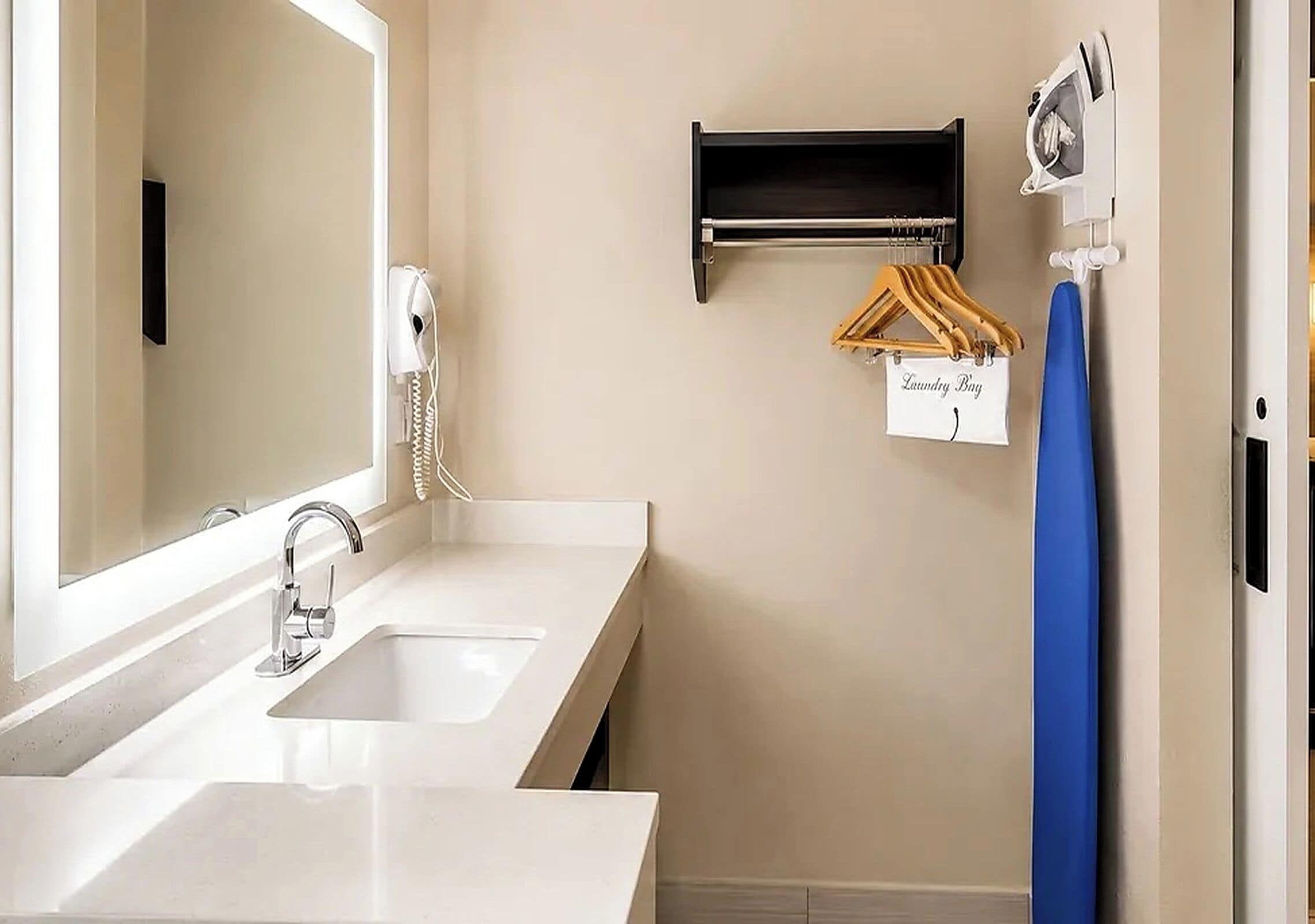 A bathroom with a double sink, a mirror, a hairdryer, a towel rack, and a laundry bag hanging on the wall.
