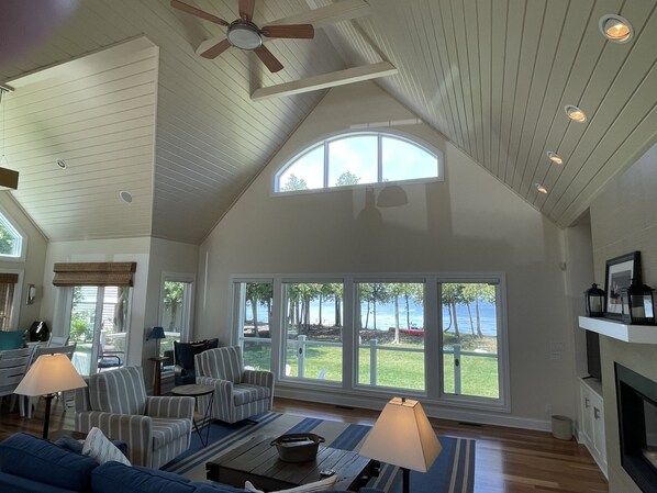 A spacious living room with a high ceiling, large windows, and a fireplace.