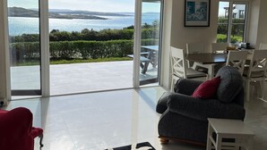 A spacious living room with a large sliding glass door leading to a patio with a view of the sea.