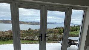 A room with a large sliding glass door leading to a patio with a view of a lake and distant hills.