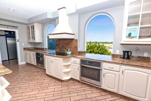 A modern kitchen with white cabinetry, a built-in oven, and a large window overlooking a landscape. - OCEANFRONT, 17 BRs, Ocean Views, Priv Pool, Rec Rm, Theatr Rm! 4x1487, The Dream (Corolla)