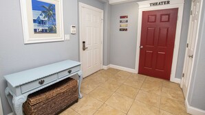 A hallway with a white door labeled "THEATER," a framed picture on the wall, and a light blue bench with baskets. - OCEANFRONT, 17 BRs, Ocean Views, Priv Pool, Rec Rm, Theatr Rm! 4x1487, The Dream (Corolla)