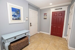 A hallway with a white door labeled "THEATER," a framed picture on the wall, and a light blue bench with baskets. - OCEANFRONT, 17 BRs, Ocean Views, Priv Pool, Rec Rm, Theatr Rm! 4x1487, The Dream (Corolla)