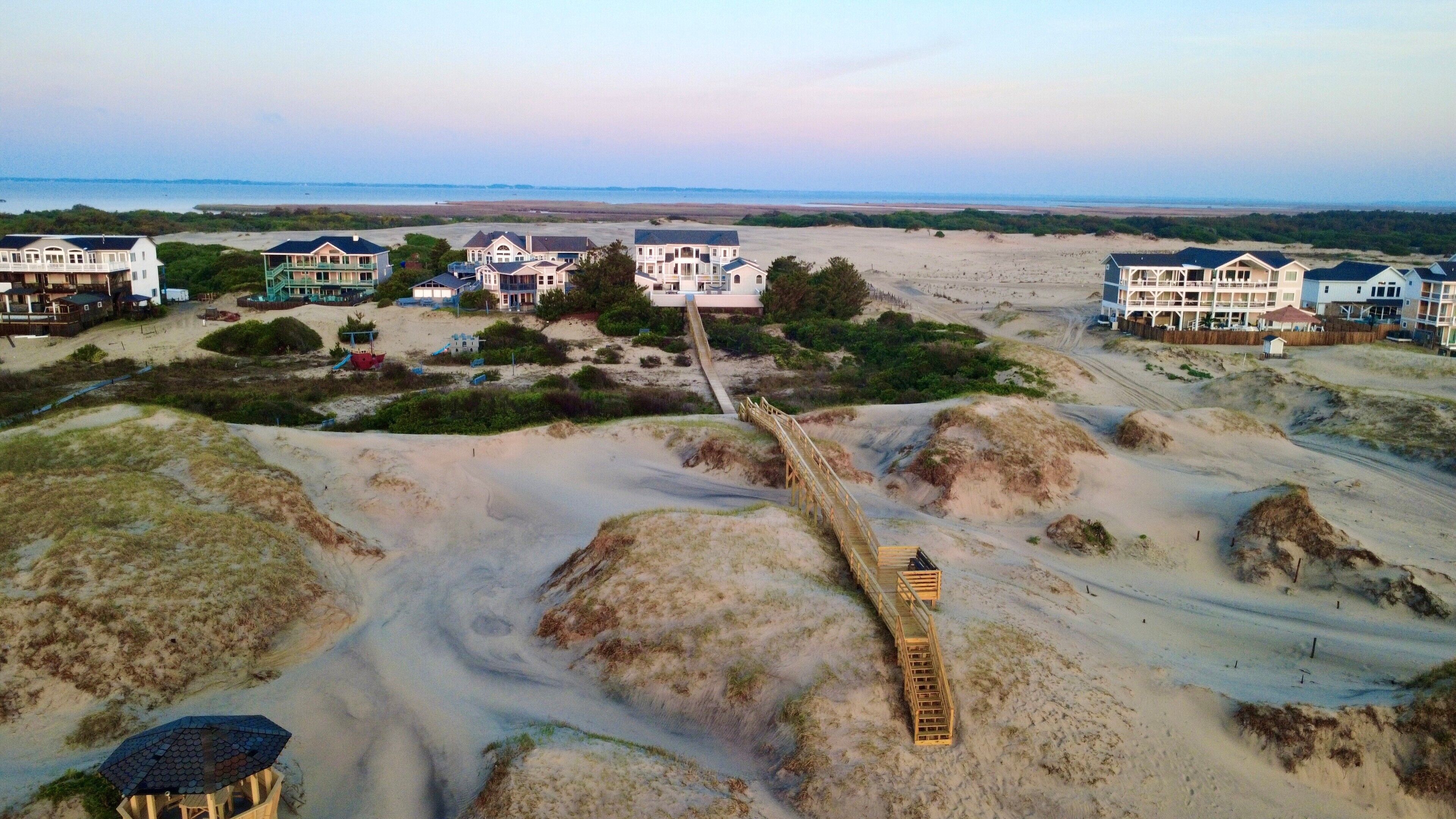 A coastal area with multiple beachfront properties, a wooden boardwalk, and sandy dunes.