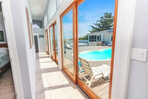 A corridor leading to a balcony with a view of a swimming pool and outdoor seating.