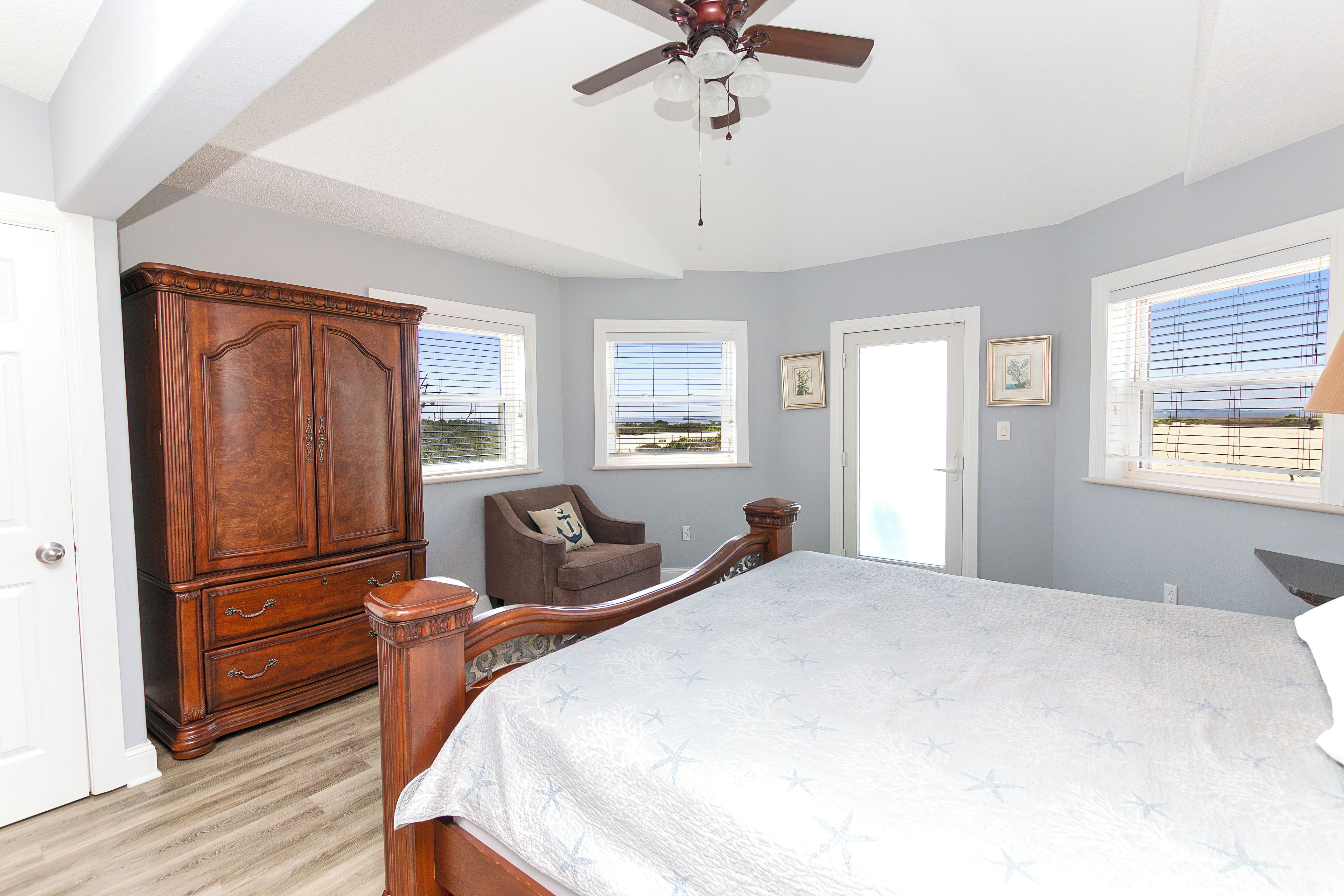 A bedroom with a large bed, a wooden wardrobe, a chair, and a ceiling fan.