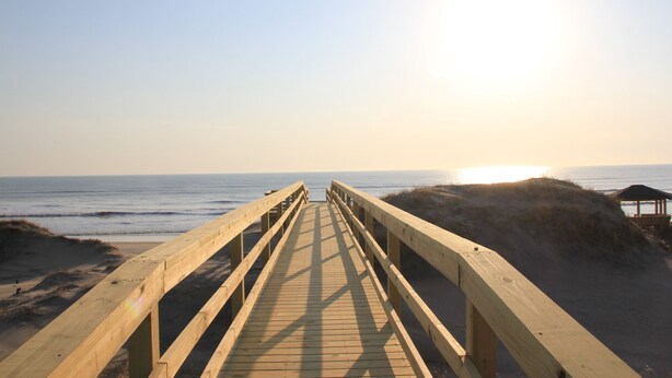 A wooden boardwalk leading to the beach with a clear view of the ocean and the sun setting in the background. - OCEANFRONT, 17 BRs, Ocean Views, Priv Pool, Rec Rm, Theatr Rm! 4x1487, The Dream (Corolla)