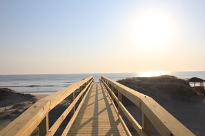 Una passerella di legno che conduce alla spiaggia, con vista libera sull'oceano e il sole che tramonta sullo sfondo.