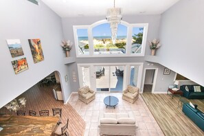 A spacious living area with a view of the beach, a chandelier, and a dining area with a table and chairs. - OCEANFRONT, 17 BRs, Ocean Views, Priv Pool, Rec Rm, Theatr Rm! 4x1487, The Dream (Corolla)