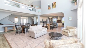 A spacious living area with a high ceiling, a dining table with chairs, a sofa, and a coffee table. - OCEANFRONT, 17 BRs, Ocean Views, Priv Pool, Rec Rm, Theatr Rm! 4x1487, The Dream (Corolla)