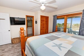 A bedroom with a bed, a ceiling fan, a TV, wooden doors, and a balcony with a view.