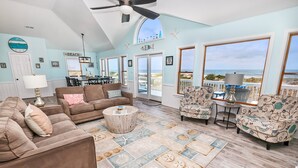 A spacious living room with a view of the beach, furnished with sofas, chairs, and a coffee table. - OCEANFRONT, Ocean Views, Private Pool, Pool Table, Dogs Welcome, OS7Q, Dune Nothin (Corolla)
