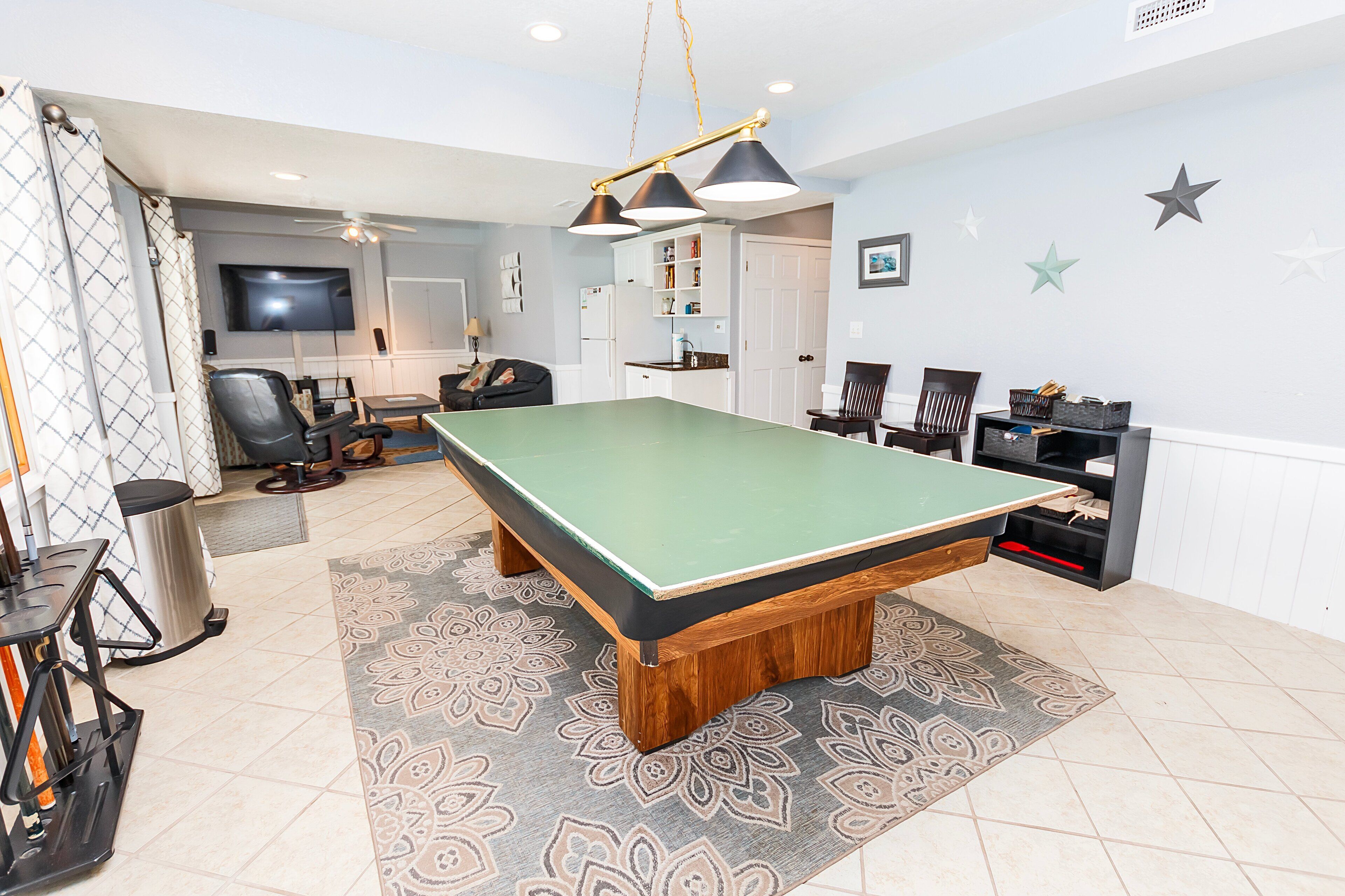 A pool table in a room with a ceiling fan, a television, and a kitchen area.
