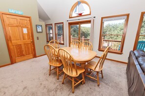 A dining area with a wooden table and chairs, a wooden door, and a view of the outdoors through large windows. - Oceanside, Private Pool, Golf Cart, Bar, Hot Tub, Rec Rm, SS4, Sunning Your Bunns (Southern Shores)