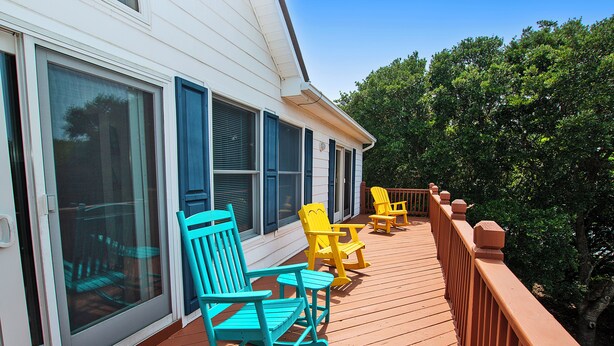 A wooden deck with rocking chairs and a table, overlooking a lush green area. - Oceanside, Private Pool, Golf Cart, Bar, Hot Tub, Rec Rm, SS4, Sunning Your Bunns (Southern Shores)