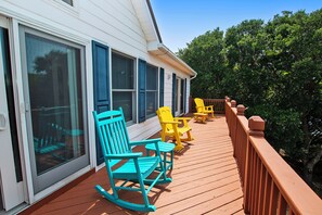 Une terrasse en bois avec des fauteuils à bascule et une table, donnant sur un espace verdoyant luxuriant.