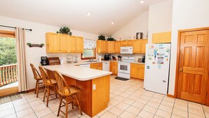 A kitchen with wooden cabinets, a central island with bar stools, a refrigerator, and a microwave. - Oceanside, Private Pool, Golf Cart, Bar, Hot Tub, Rec Rm, SS4, Sunning Your Bunns (Southern Shores)