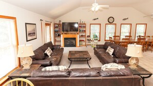 A spacious living room with leather sofas, a fireplace, a TV, and a dining area with wooden chairs and a table. - Oceanside, Private Pool, Golf Cart, Bar, Hot Tub, Rec Rm, SS4, Sunning Your Bunns (Southern Shores)