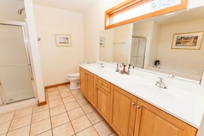 A bathroom with a white sink, wooden cabinets, a large mirror, and a shower. - Oceanside, Private Pool, Golf Cart, Bar, Hot Tub, Rec Rm, SS4, Sunning Your Bunns (Southern Shores)