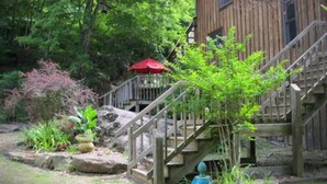 Una baita di legno con una scala in pietra che conduce a un patio, immersa nel verde e con un piccolo ombrello rosso.