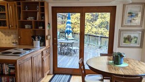Una cucina con mobili in legno, un tavolo da pranzo con sedie, un'ampia finestra vista su un patio e alberi, e un lampadario.