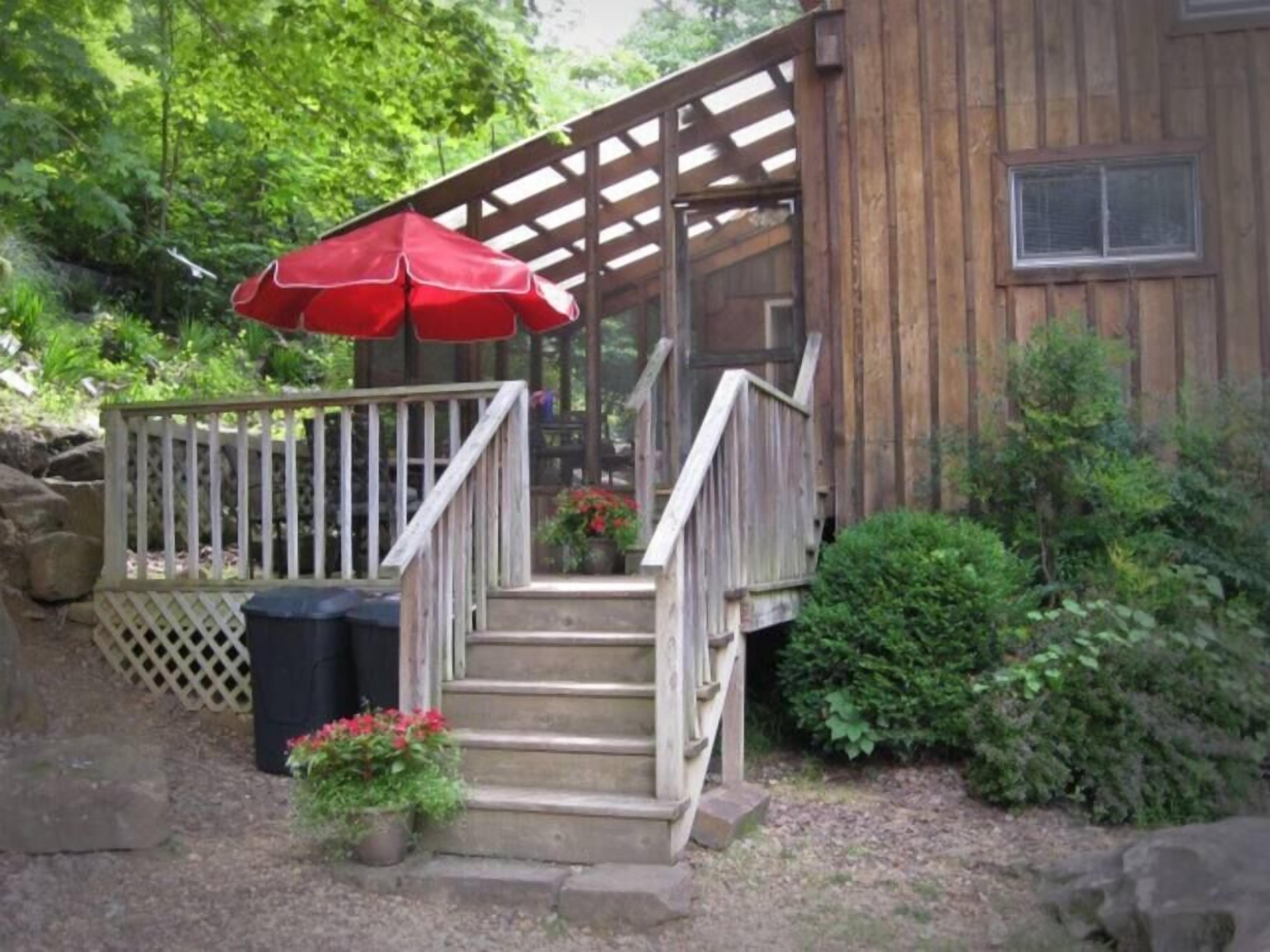 A wooden cabin with a wooden deck and a red umbrella.