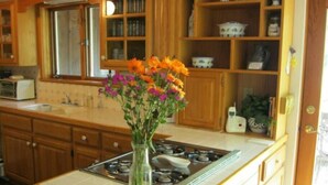 Cucina con pensili in legno, piano cottura a gas, lavello e vaso con fiori sul ripiano.