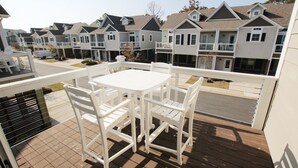A balcony with a white table and chairs, overlooking a row of townhouses with gabled roofs and front porches. - Oceanside, Patio, Hot Tub, Rec Room, BV8A, Break Away (Corolla)