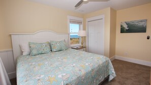 A bedroom with a bed, a nightstand, a lamp, a window with a view, a door, and a painting on the wall. - OCEANFRONT, Ocean Views, Private Beach Walkway! NH1, Blackbeard's JEM (Nags Head)