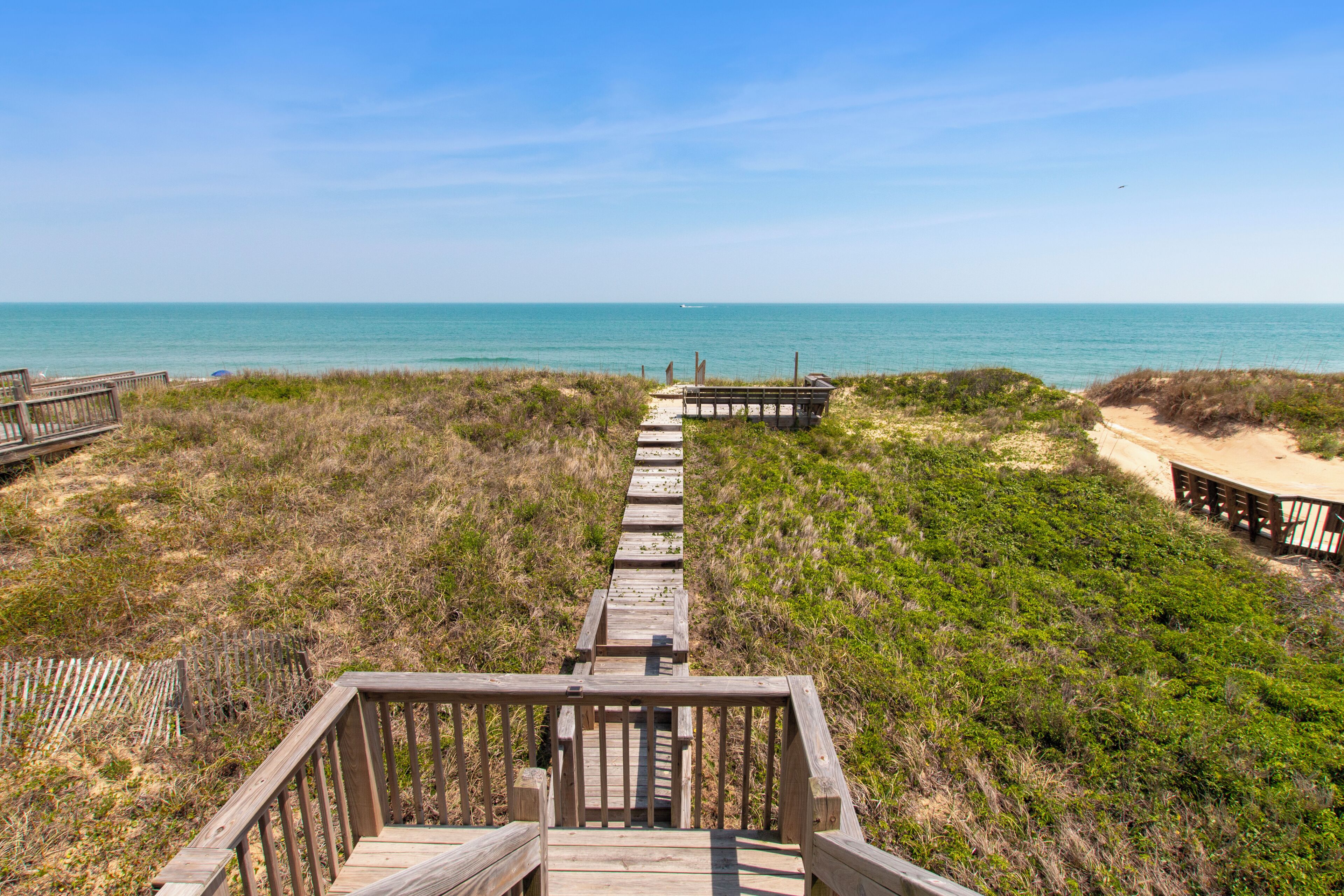 A wooden boardwalk leading to a beach with dunes and a clear sky.