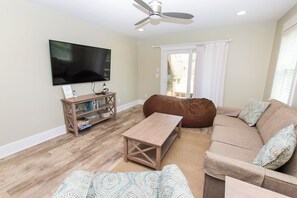 A living room with a flat-screen TV, a wooden coffee table, a brown sofa, and patterned cushions.