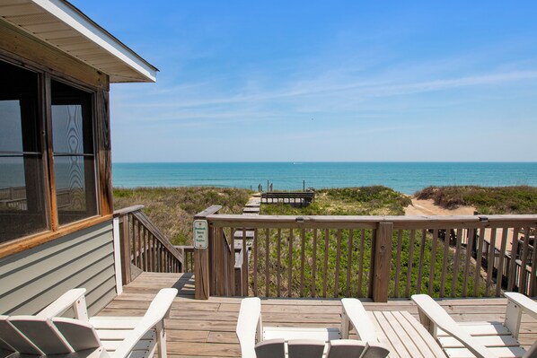 A wooden deck with white chairs, a wooden railing, and a view of the ocean.
