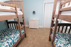 Una habitación con literas, un pequeño aparador blanco y una puerta.