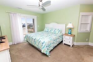 A bedroom with a bed, a nightstand, a lamp, a ceiling fan, and a view through a window.