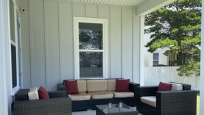 A covered patio with a beige sectional sofa, two armchairs, and a coffee table.